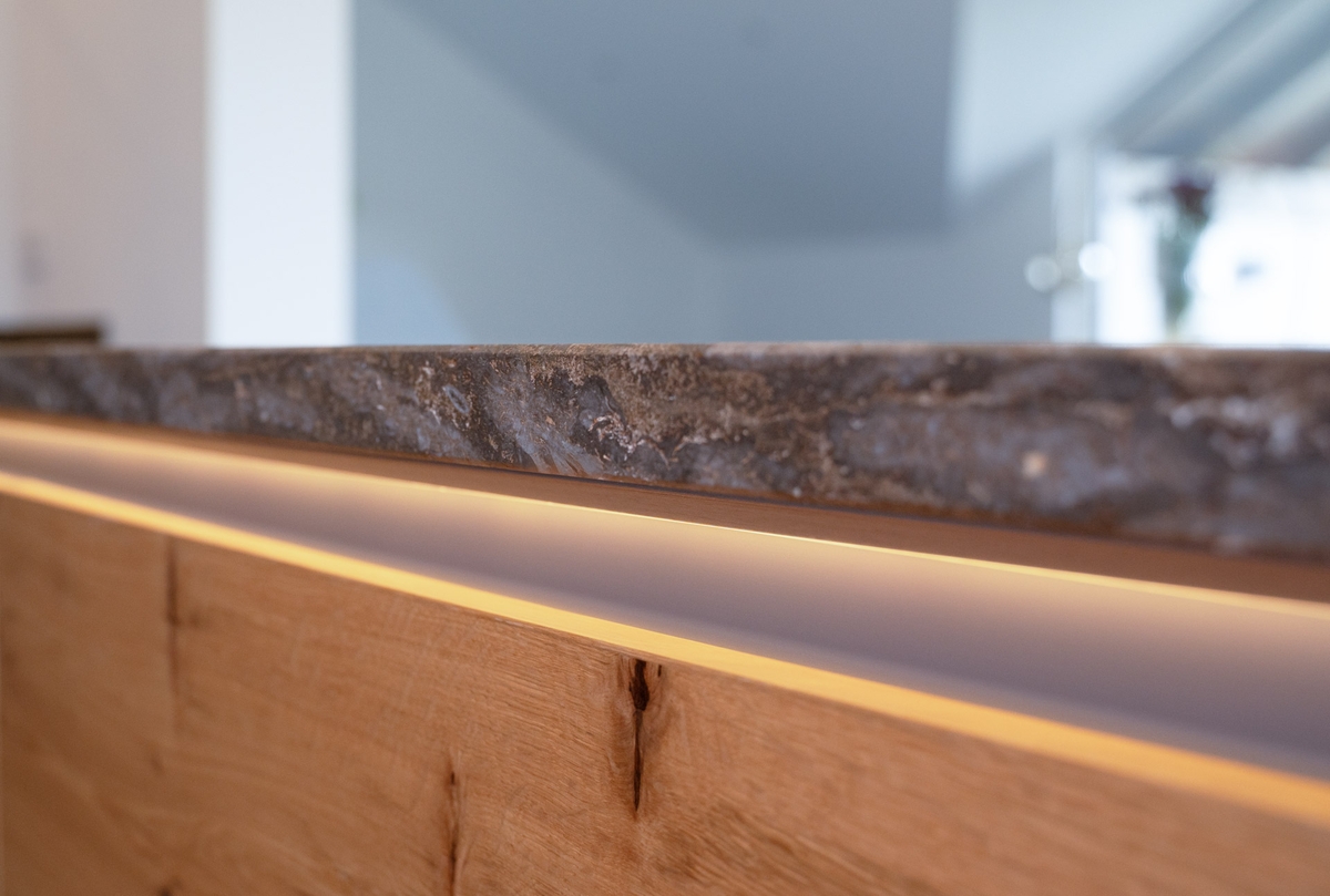 Detailaufnahme einer Naturstein-Arbeitsplatte mit integrierter Lichtleiste und Holzfront von Baumann Küchen