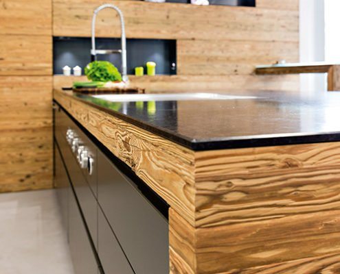 Küchenstudio Baumann - Eine moderne Kochinsel aus Echtholz mit einer glatten schwarzen Granit Arbeitsplatte.