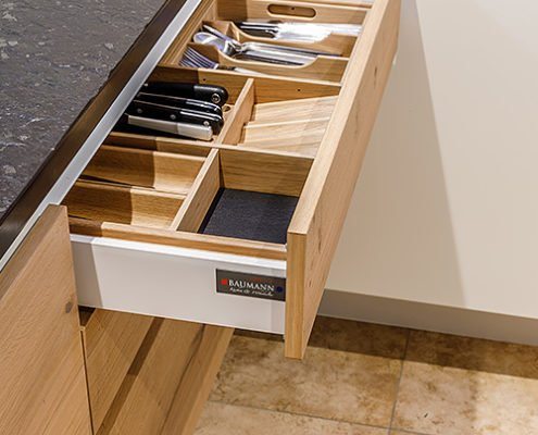 Baumann Küche Ebersberg - Eine ausgezogene Küchenschublade aus hochwertigem Echtholz mit verschiedenen Trennelementen für Besteck und andere Küchen Utensilien.