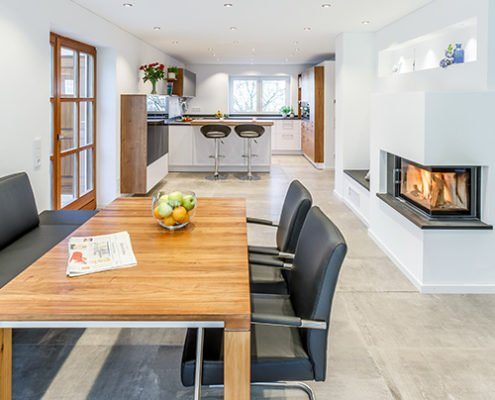 Baumann Küchen - Entfernte Sicht auf eine helle, moderne Küche vom Essbereich aus, mit viel Echtholz und weißen Elementen.