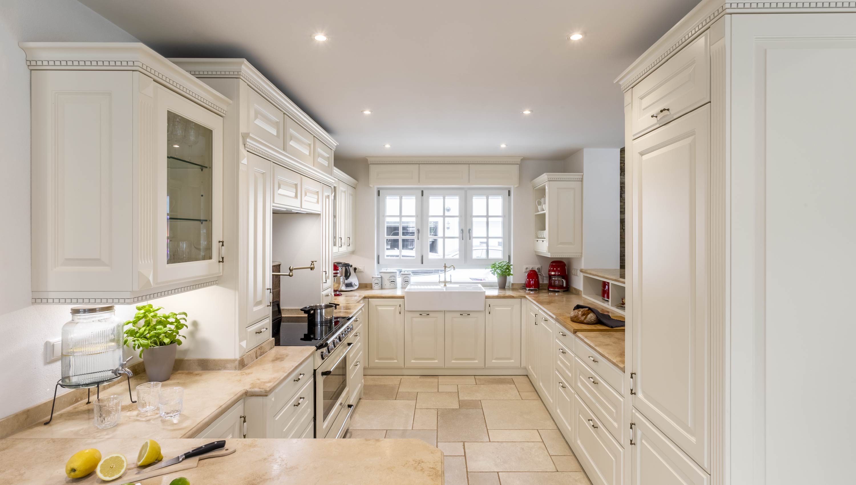 Baumann Küchen - Eine helle hochwertige Landhaus Küche mit weißen Fronten und einer Marmor Arbeitsplatte.